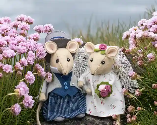 Felt mouse bride and groom wedding toppers standing among pink flowers
