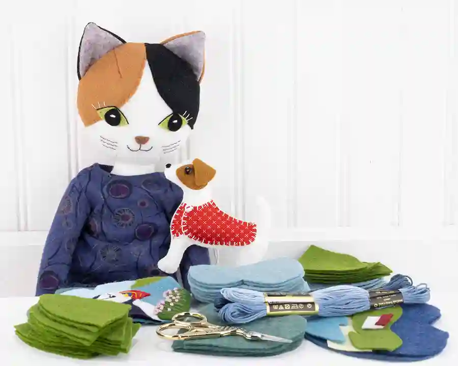 Puffin the cat and Jip the Jack Russell sitting in a workspace with threads, scissors and piles of cut felt pieces