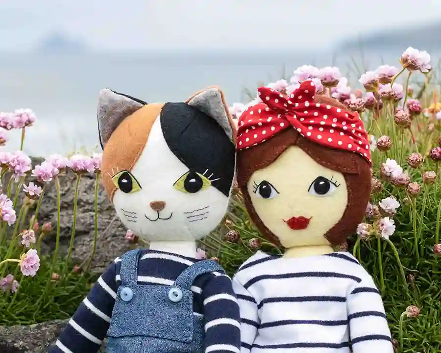 Tilly doll and Puffin cat sitting among the sea pink flowers beside the sea
