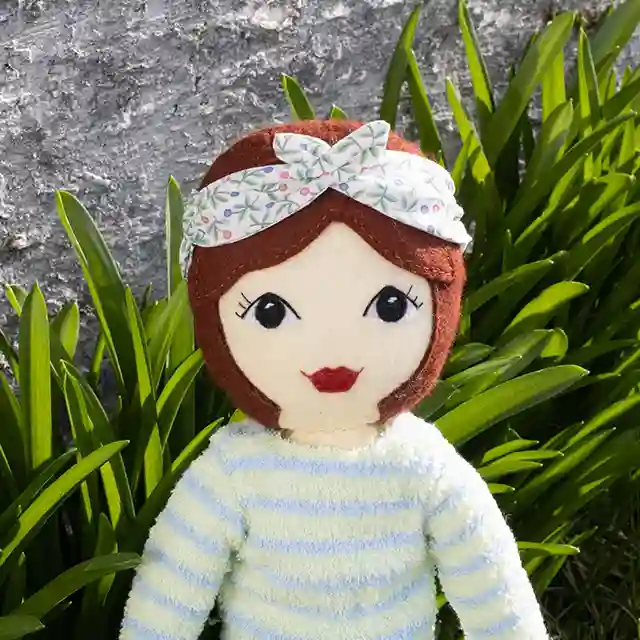 Tilly the felt doll sitting in a garden.
