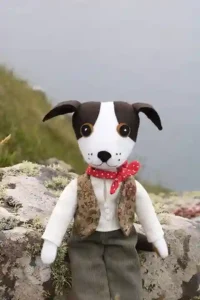 Toby the felt dog sitting on a lichen-covered rock beside the sea