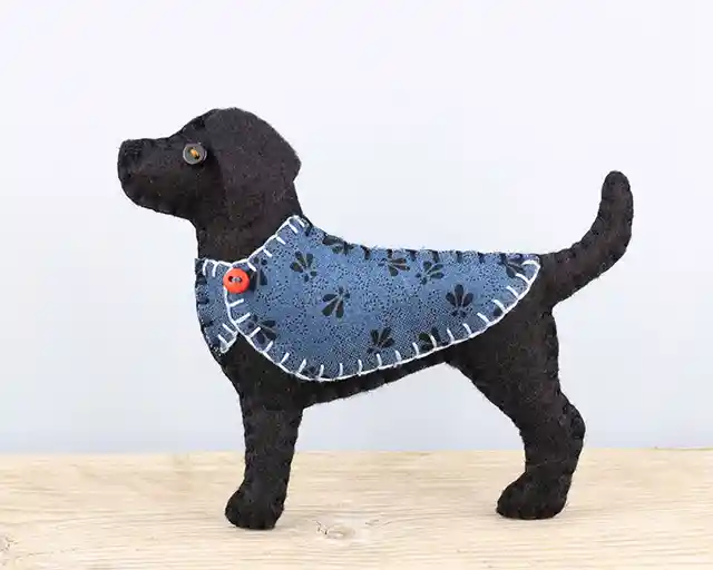 A black Labrador felt ornament wearing a blue patterned jacket with a red button