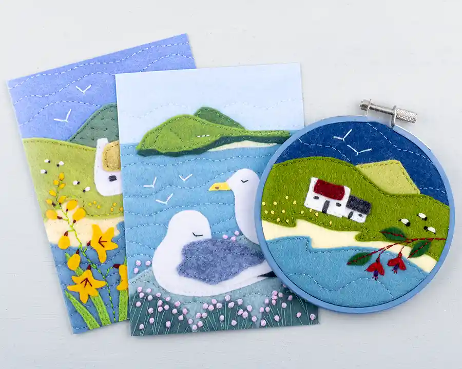 An embroidered felt Irish landscape framed in a painted hoop, with greeting cards printed with embroidered felt scenes