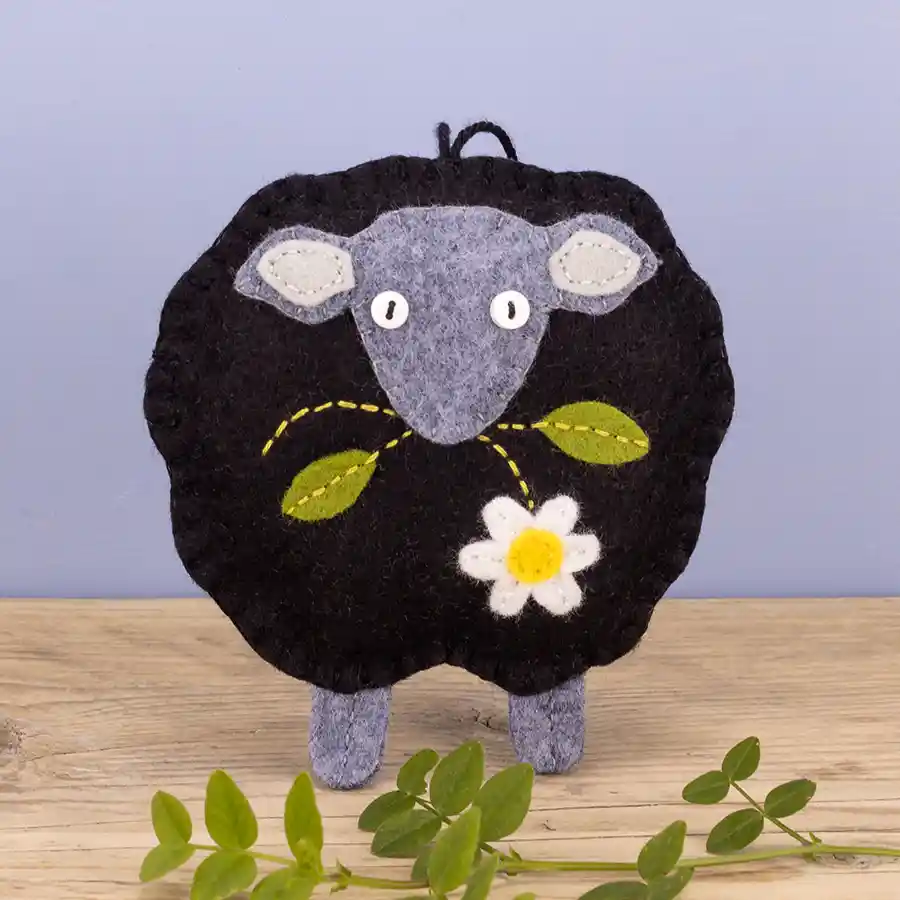 A black sheep felt ornament with light grey head and legs and a daisy flower with two leaves.