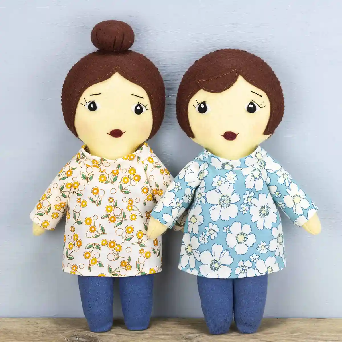 Two Daisy dolls, one with a bob hairstyle and one with a ballerina-style bun. There hair is made of felt and they wear floral-print cotton tunics in blue, yellow and white, and blue stretch tights.