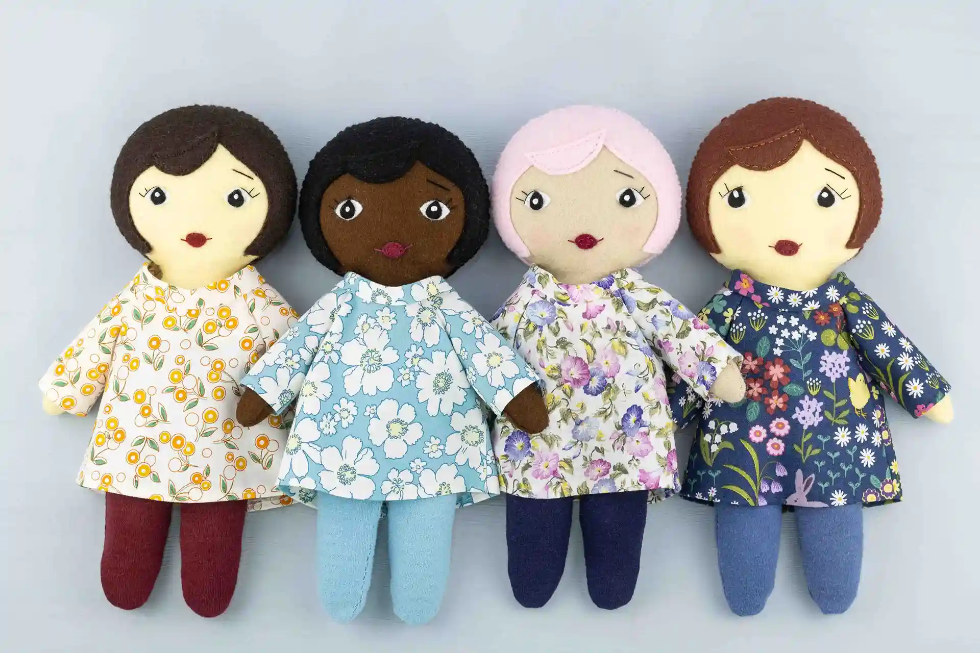 A row of four Daisy dolls with different hair colours and skin tones, wearing floral print tunics and jersey tights.