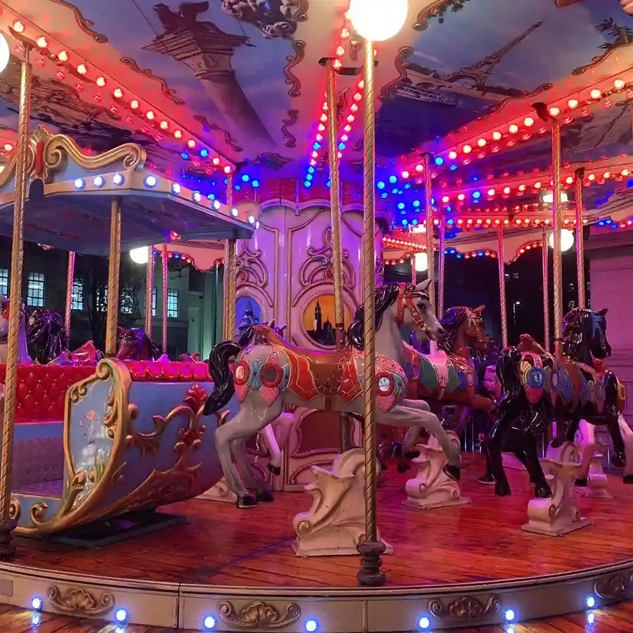 Close-up of a colourful carousel showing carved wooden horses and gold poles.