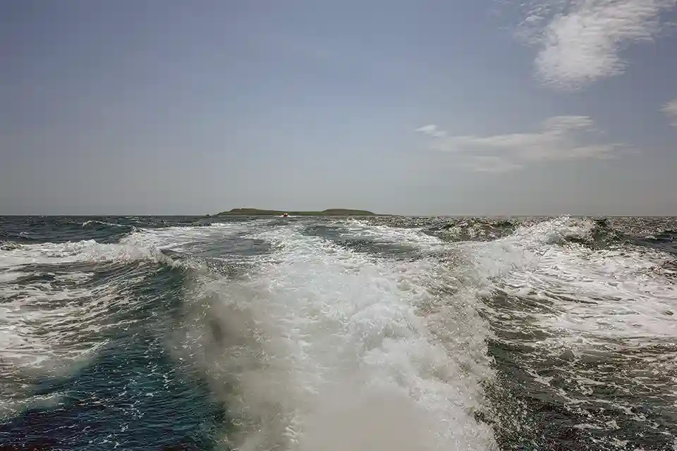 View of the distant island from the stern of the boat, with foaming wake.
