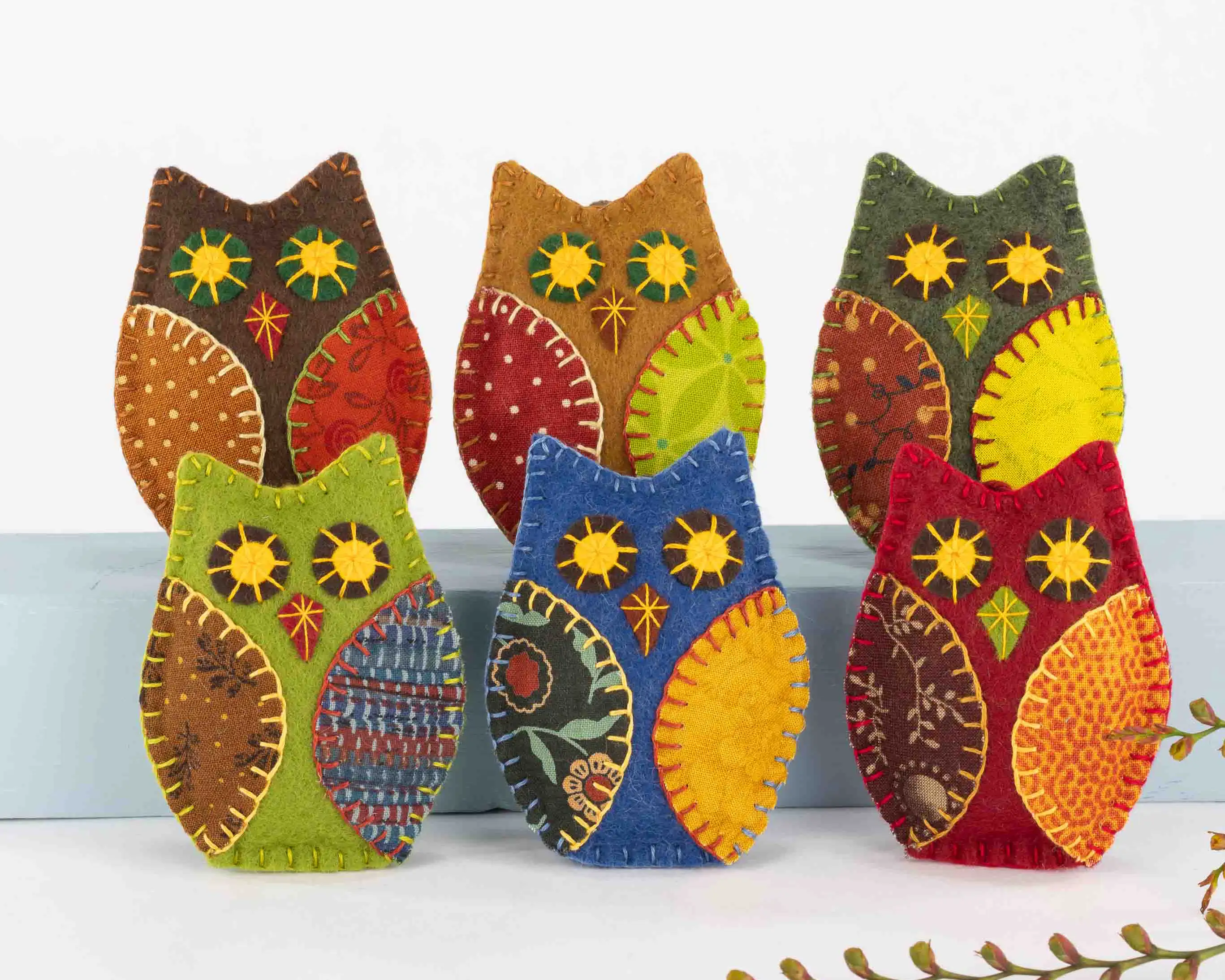 Six felt owl ornaments in autumnal colours with appliqued wings of patterned fabric and embroidered eyes and beaks.