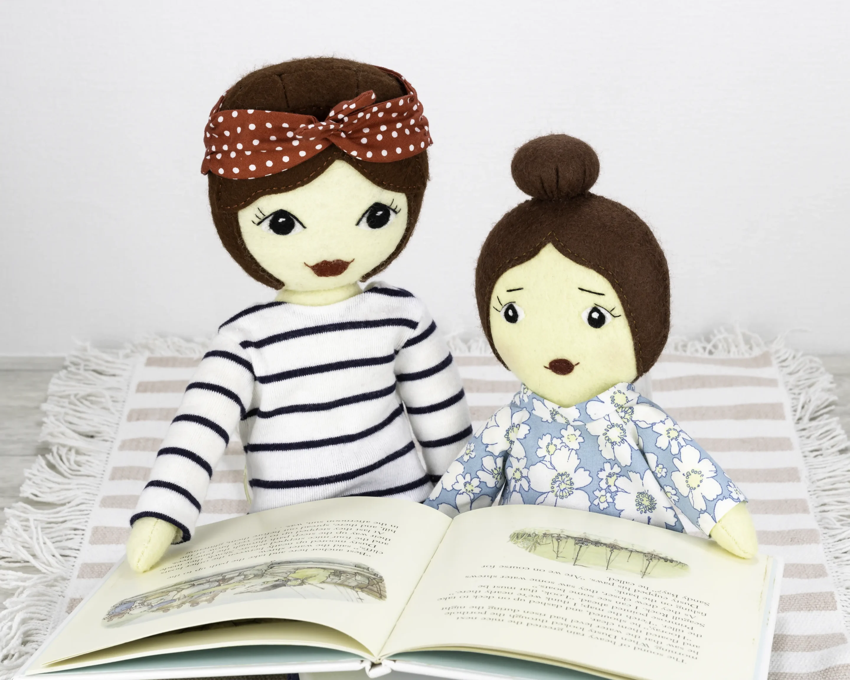 Two Daisy dolls, one with a bob hairstyle and one with a ballerina-style bun. There hair is made of felt and they wear floral-print cotton tunics in blue, yellow and white, and blue stretch tights.