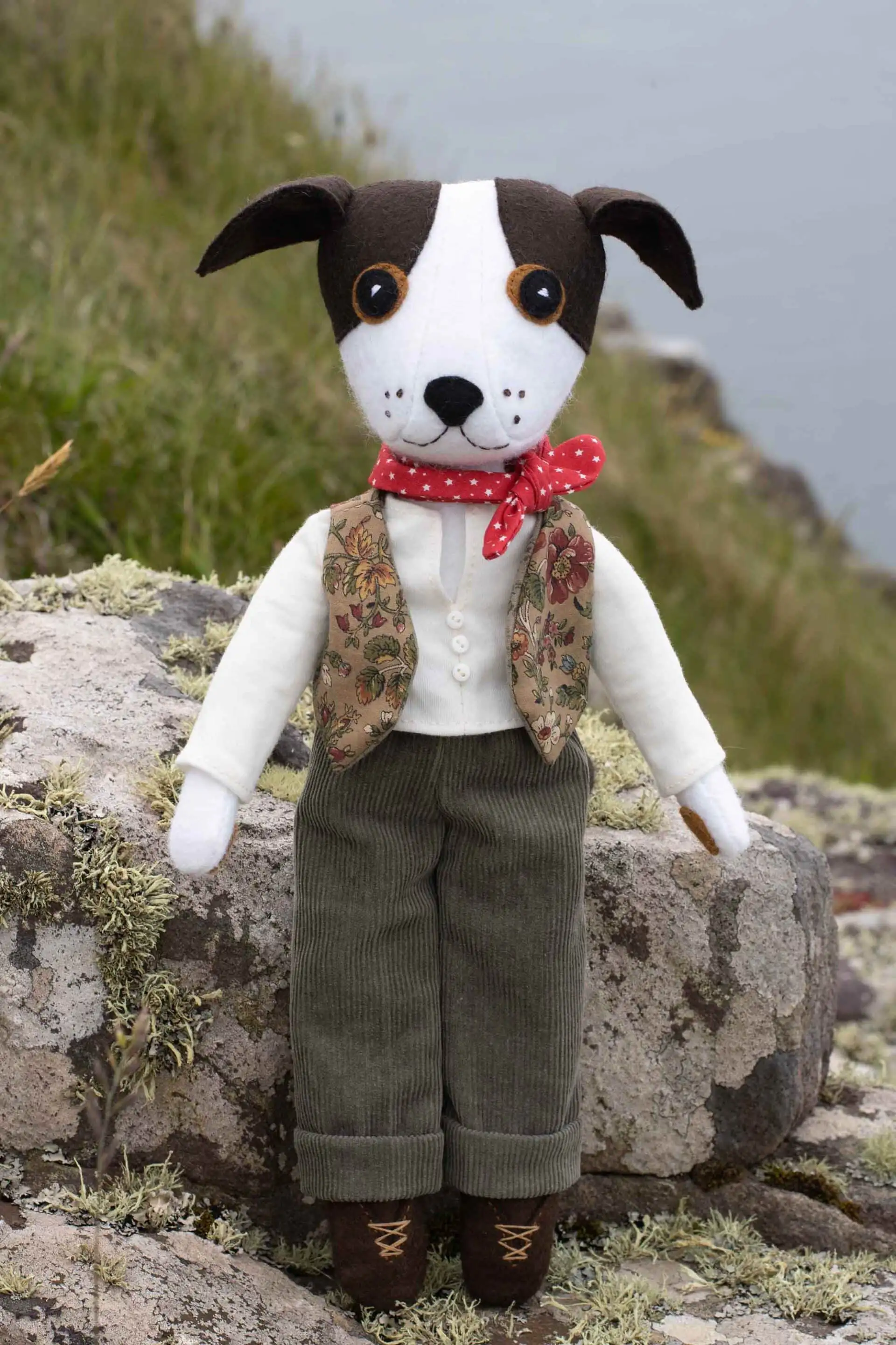 Toby the felt dog sitting on a lichen-covered rock beside the sea