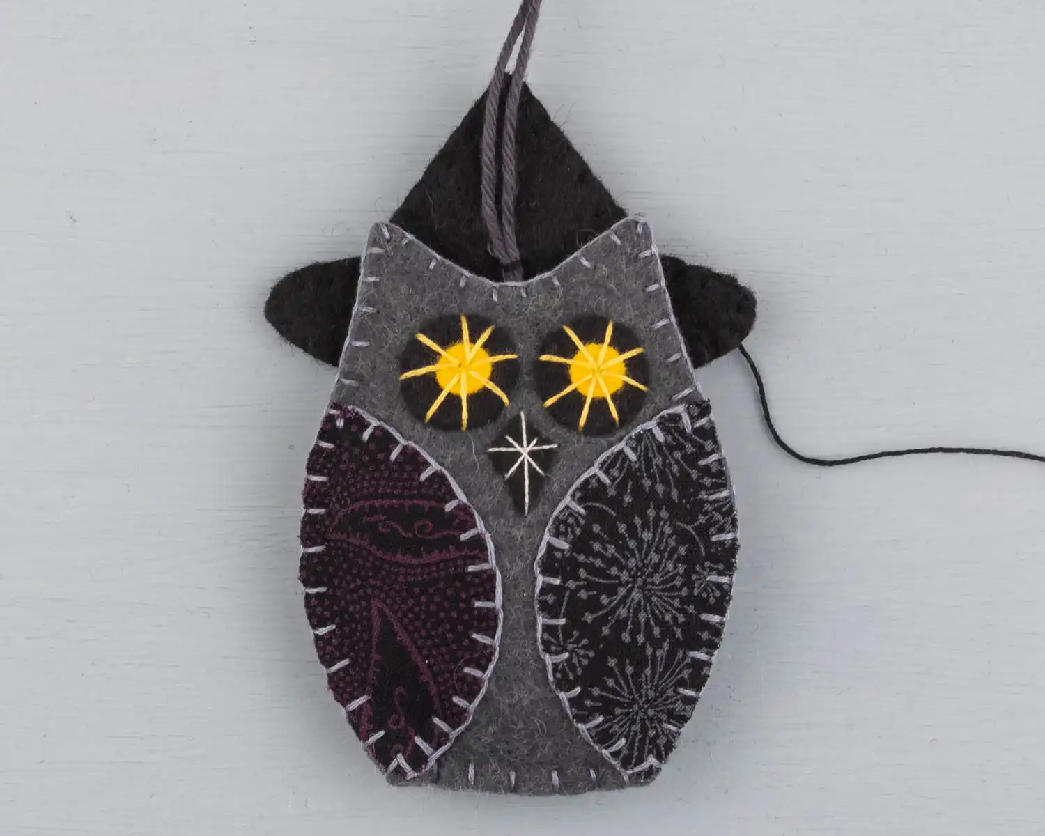 Showing the owl from the front, stitching the hanging loop to the hat.