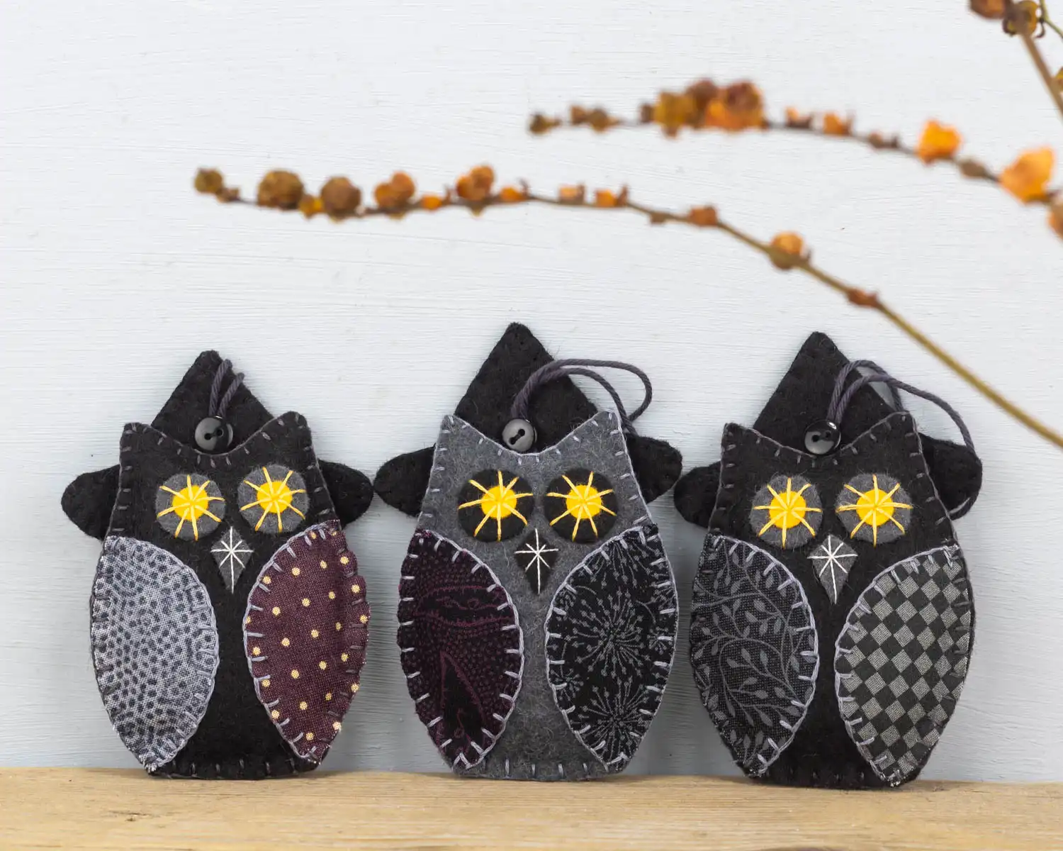 Three felt owl ornaments in black and grey with patterned fabric wings, wearing black felt witch hats